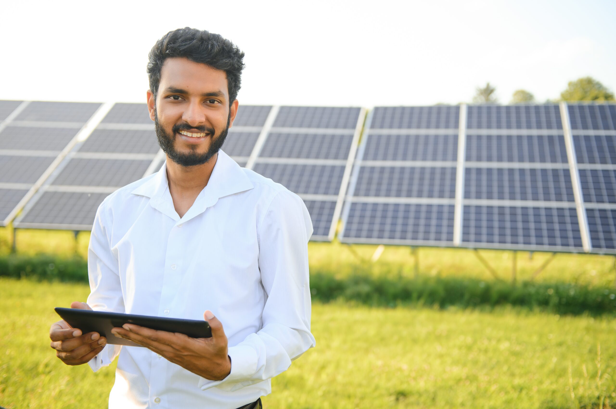 Portrait of Young indian male engineer standing near solar panels, with clear blue sky background, Renewable and clean energy. skill india, copy space